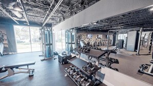 Un gimnasio con diverso equipo de ejercicio, como mancuernas, una banca y máquinas de cardio.