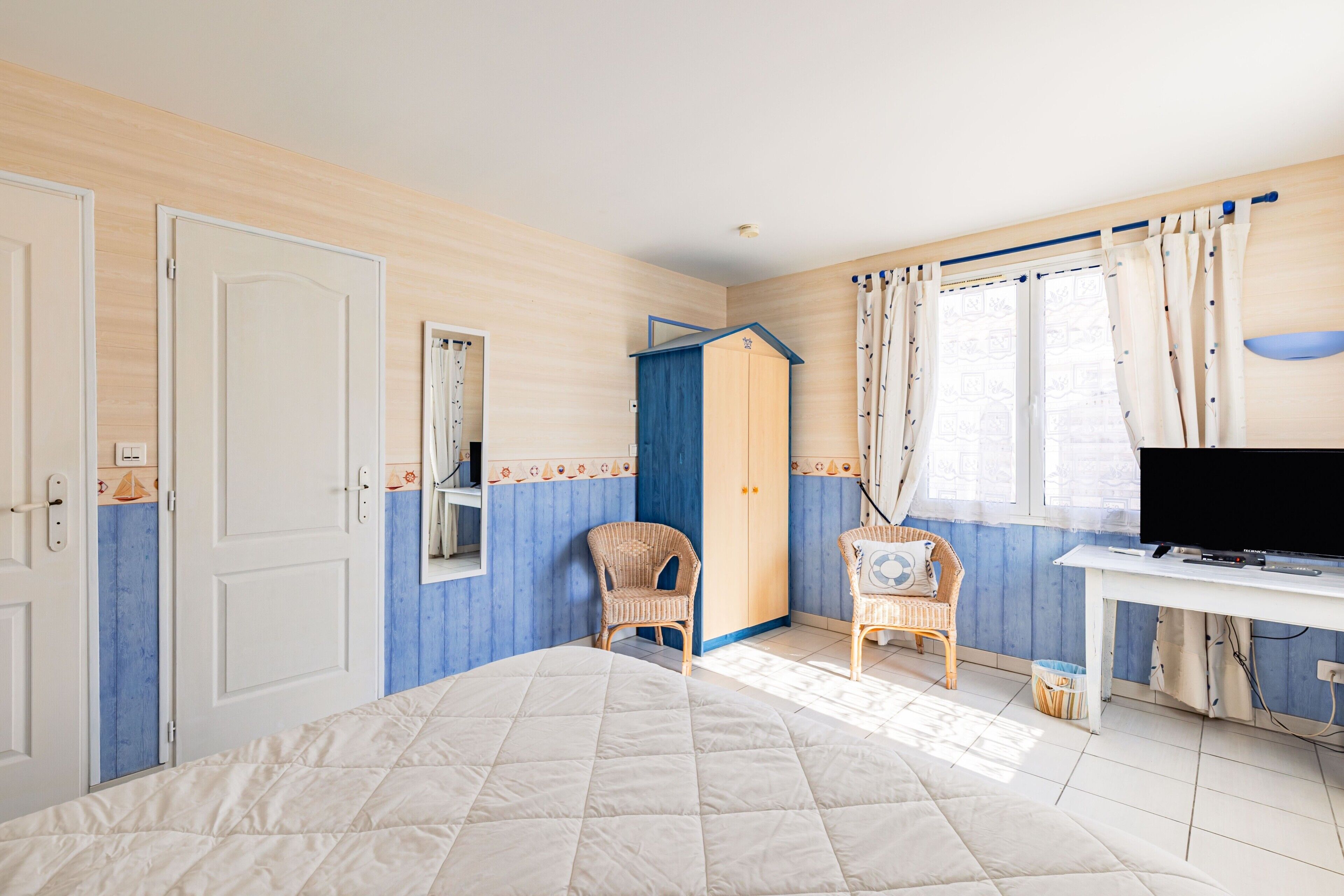 Une chambre à coucher avec un lit, une armoire, une télévision et une fenêtre avec des rideaux.