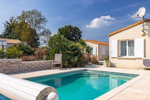 A swimming pool with a stone wall, a chair, and a building with a satellite dish.