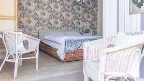 A bedroom with a bed, two white wicker chairs, a patterned wallpaper, and a hanging light fixture. - Guest Room “Fidji” with Shared Pool, Wi-Fi, and Air Conditioning (Saint-Pierre-d'Oléron)