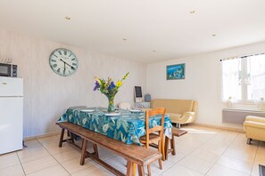 A dining area with a wooden bench, a table with a tropical leaf tablecloth, a clock, and a vase with flowers.