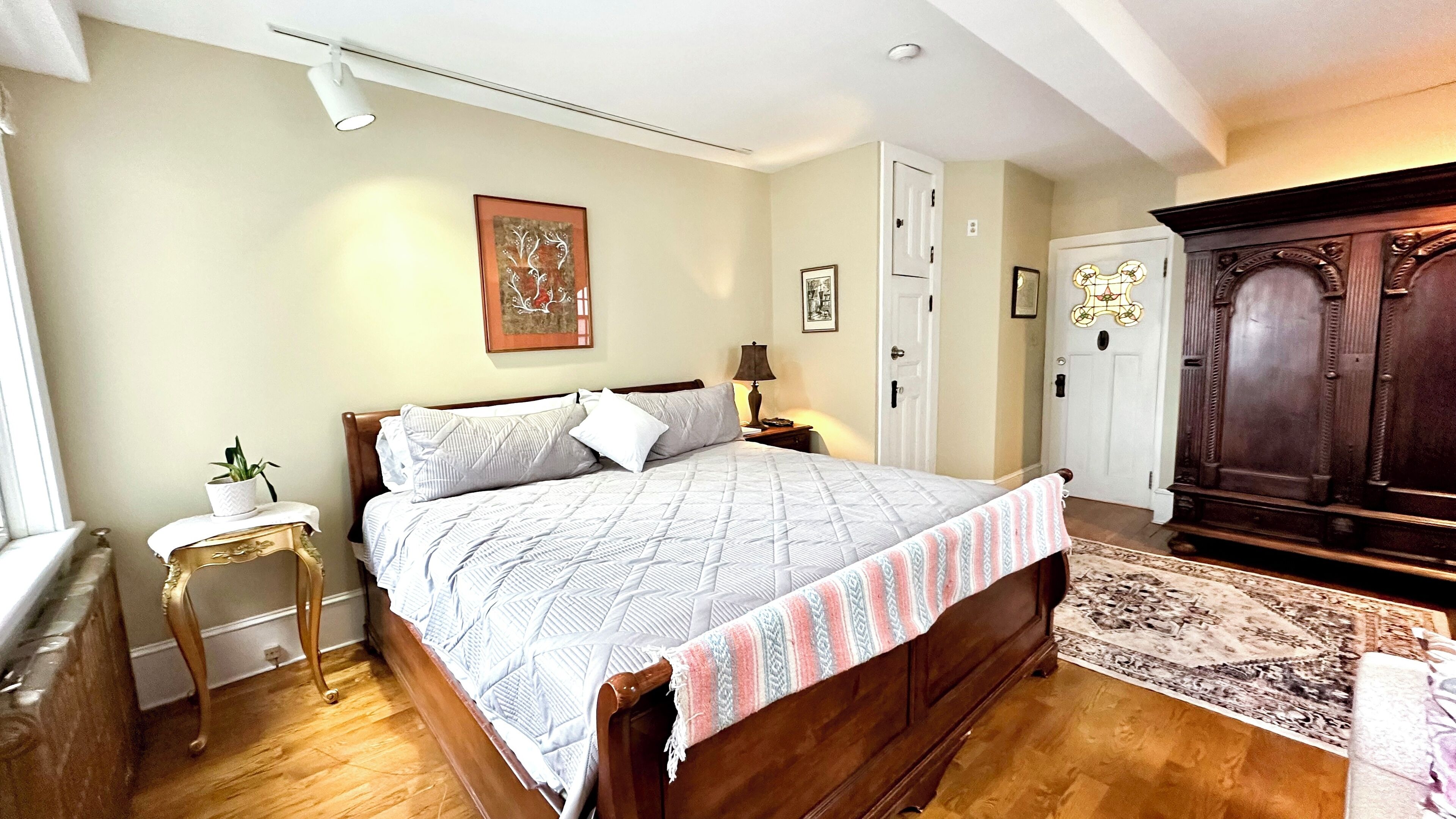 Een slaapkamer met een houten bed, een nachtkastje met een lamp, een kleine potplant en een grote houten garderobe.