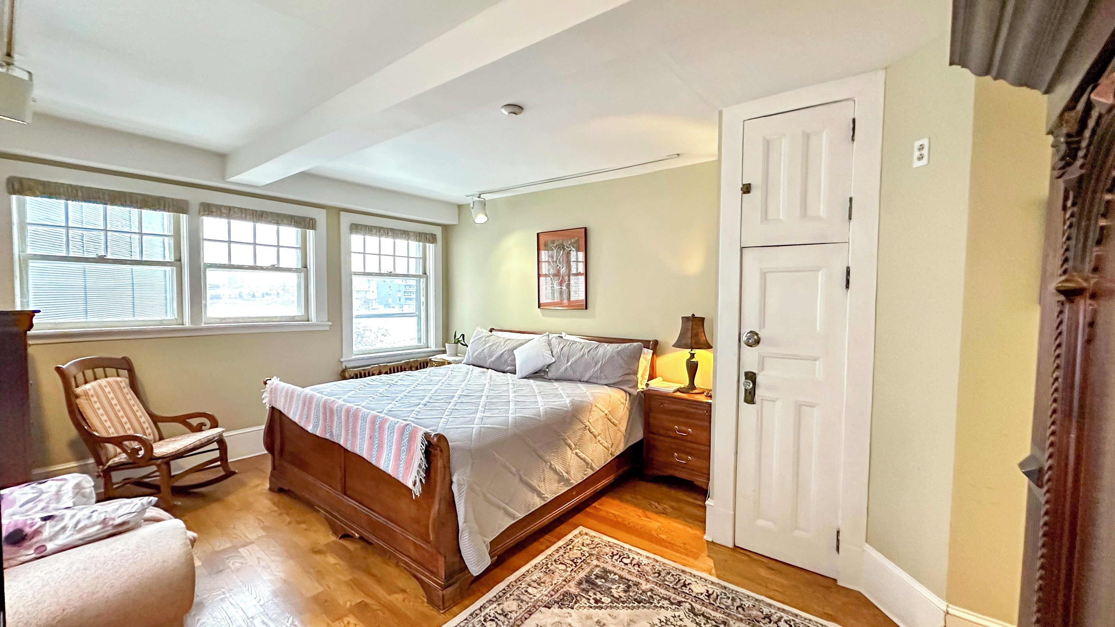 A bedroom with a large bed, a chair, a nightstand, and a door.