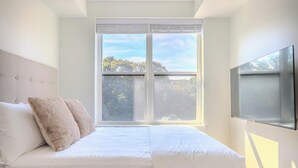 Une chambre à coucher avec un lit, une fenêtre avec des stores et un téléviseur fixé au mur.