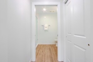 A narrow hallway leading to a bathroom with a toilet and a towel hanging on the wall. - Landing | Modern 1BD, Gym (Ithaca)