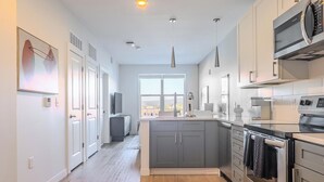 A modern kitchen with grey cabinets, stainless steel appliances, and a large window providing natural light.