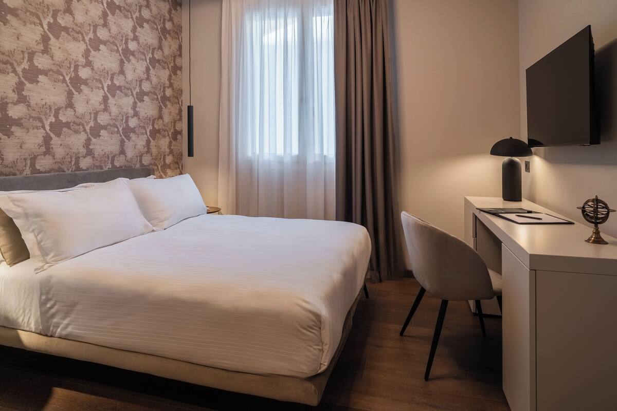 Ein modernes Hotelzimmer mit einem großen Bett, einem Schreibtisch und einem an der Wand befestigten Fernseher.