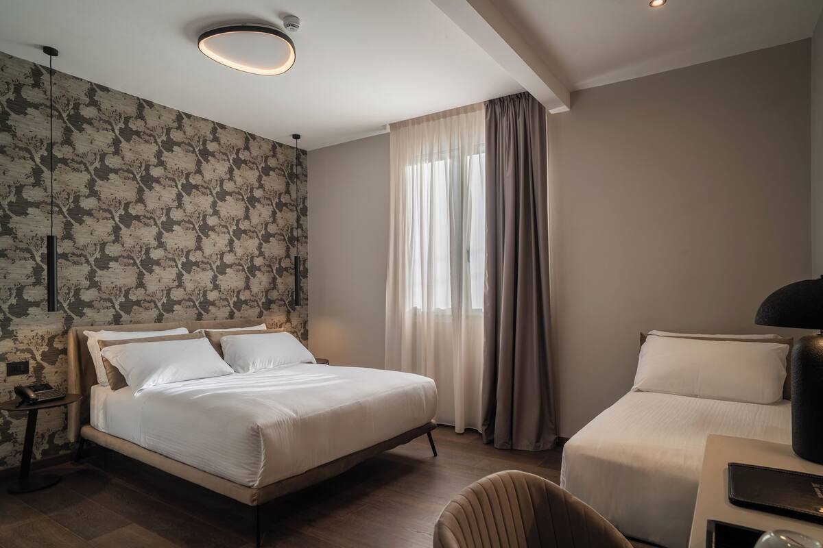 Ein Hotelzimmer mit einem großen Bett, einem kleineren Bett, einem Schreibtisch mit Lampe und einem Sessel.