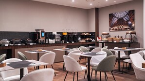 Un café moderne doté d’un espace dédié à la préparation du café, d’un coin salon et d’une grande œuvre d’art représentant un paysage urbain, accrochée au mur.