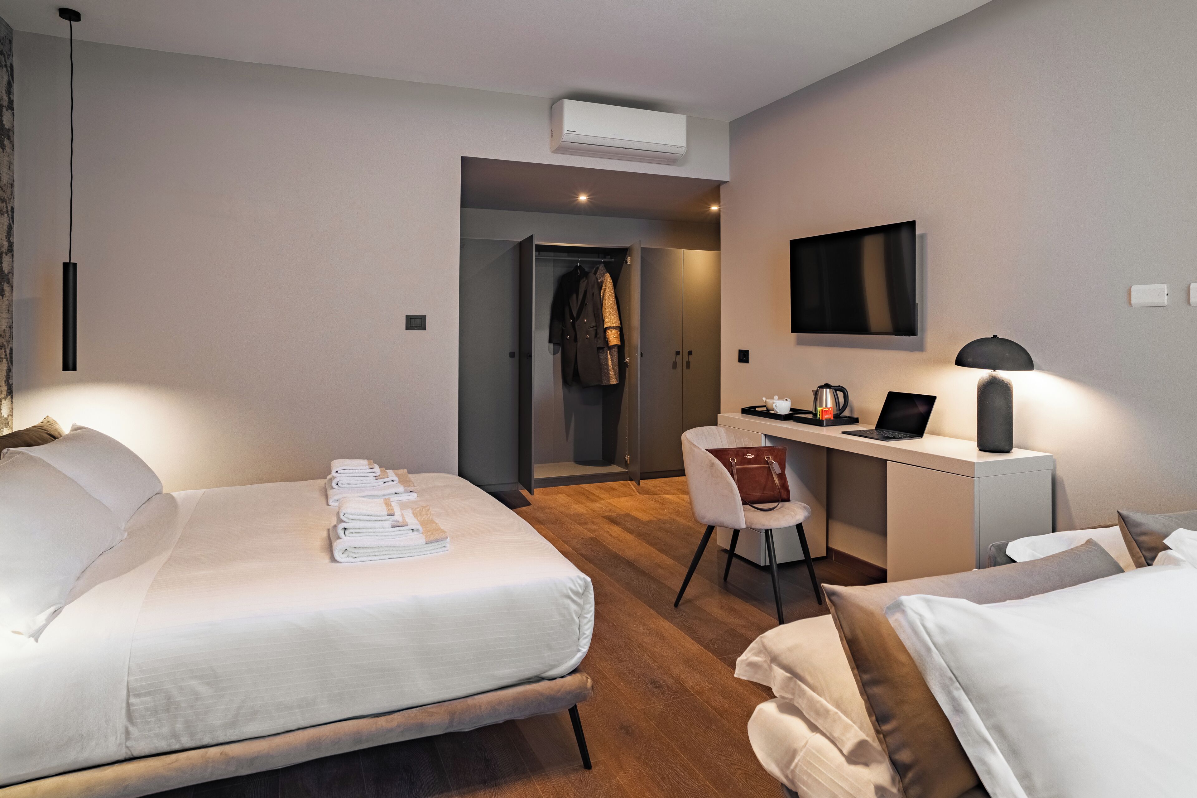 A modern hotel room with a bed, a desk with a laptop, a chair, and a TV mounted on the wall.