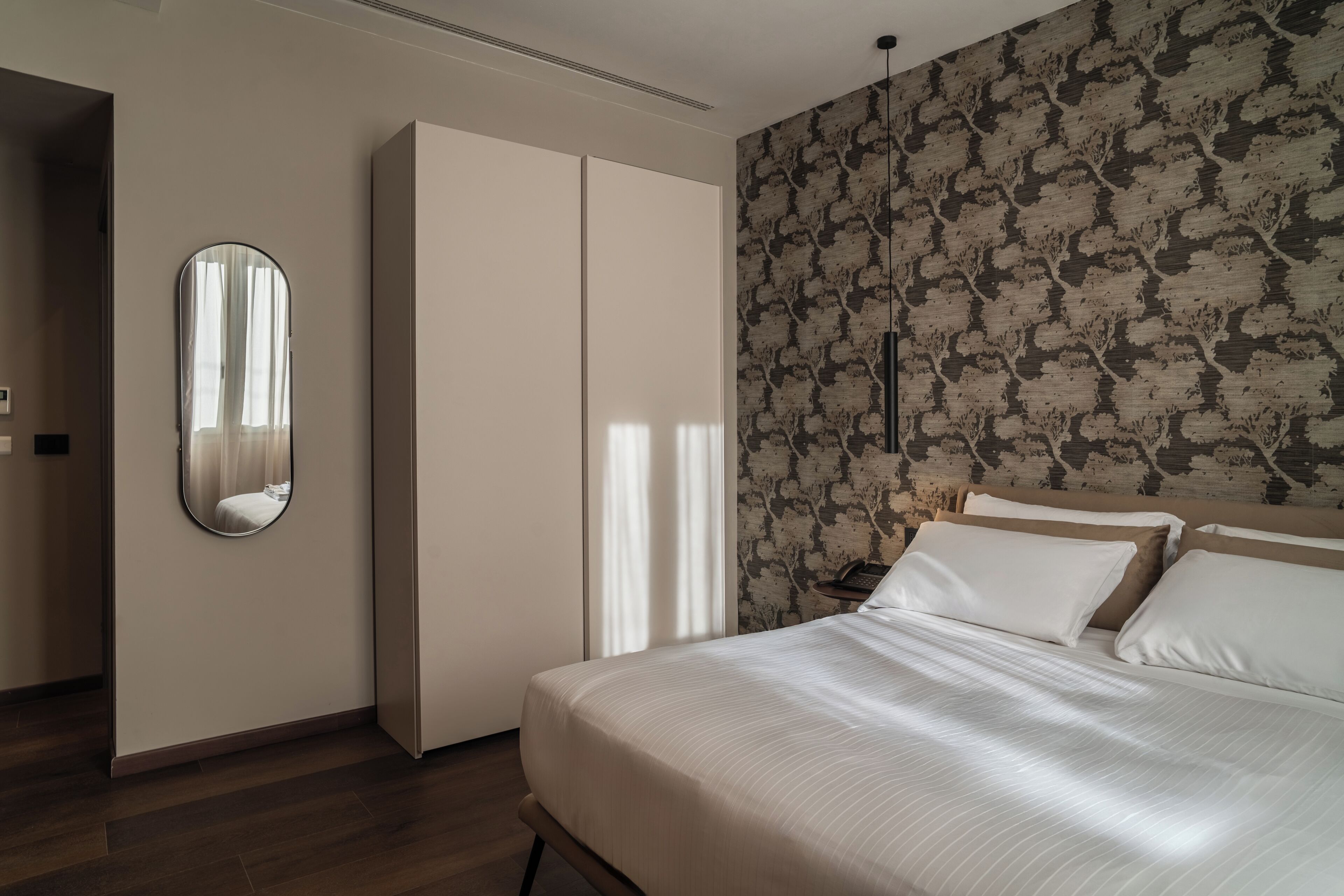 A bedroom with a bed, a wardrobe, a mirror, and a patterned wall.