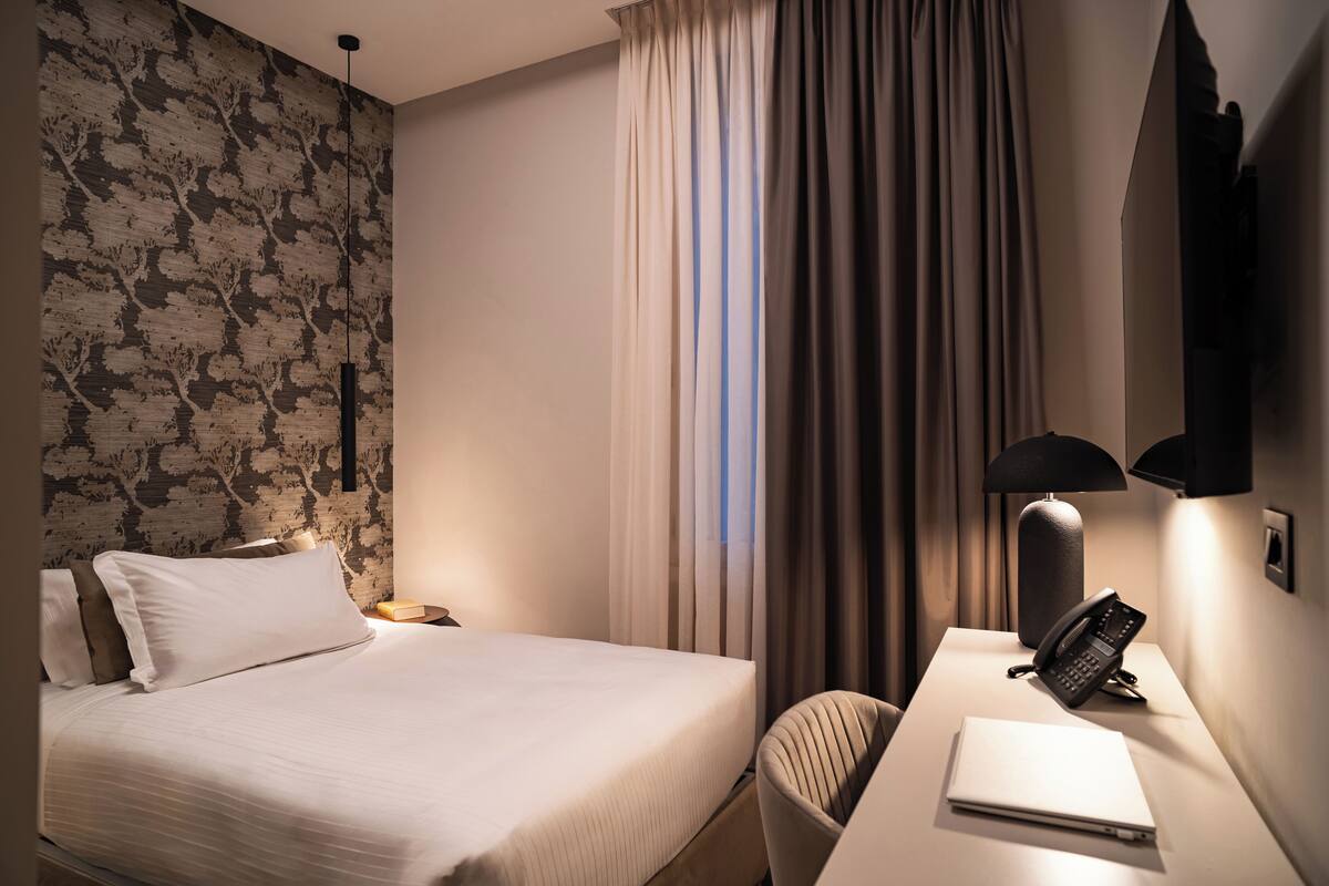 Ein Hotelzimmer mit einem Bett, einem Schreibtisch mit Lampe, einem Telefon und einem Sessel.