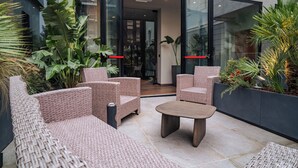 Un espace extérieur moderne, aménagé avec des meubles en osier et une table basse centrale, le tout entouré d’une végétation tropicale luxuriante.