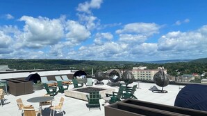 A rooftop terrace with outdoor seating, including chairs and tables, and a view of the surrounding landscape.