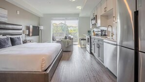 Ein modernes Hotelzimmer mit einem großen Bett, einer Küchenzeile und einem Balkon mit Blick auf die Stadt.