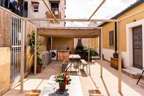 A covered outdoor patio with a table and benches, surrounded by potted plants and a washing machine. - Casa Giusi Terrace Charm by Wonderful Italy (Catania)