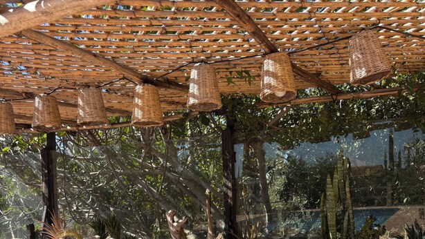 Een terras met buitenmeubilair van riet, een houten pergola en uitzicht op bomen en een zwembad.