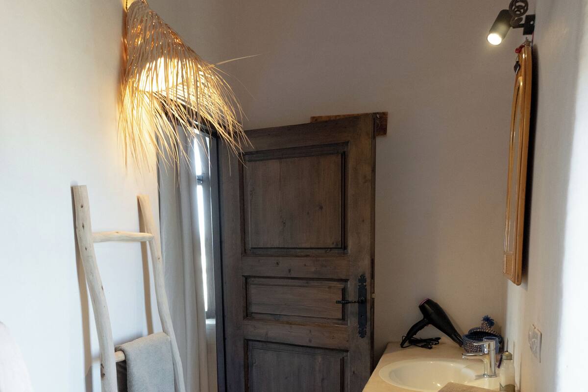 Une salle de bain avec des toilettes blanches, une échelle en bois, un lavabo blanc avec une serviette et une porte en bois.