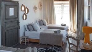 Een knus ingerichte kamer met een rustieke plafond, twee bedden, een houten stoel, een tafeltje en een raam met gordijnen.