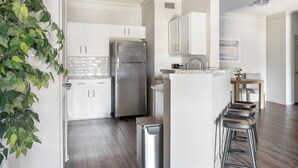 A modern kitchen with white cabinets, a stainless steel refrigerator, and a bar stool area. - Landing | Stunning 1BD, Gym, Tennis Court (Stockbridge)