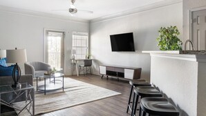 A modern living room with a flat-screen TV, a dining area with a table and chairs, a kitchen with a sink and countertop, and a staircase leading to another level. - Landing | Stunning 1BD, Gym, Tennis Court (Stockbridge)