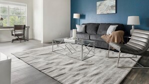 Una sala de estar moderna con un sofá gris, un sillón de cuero y una mesa de centro de vidrio.