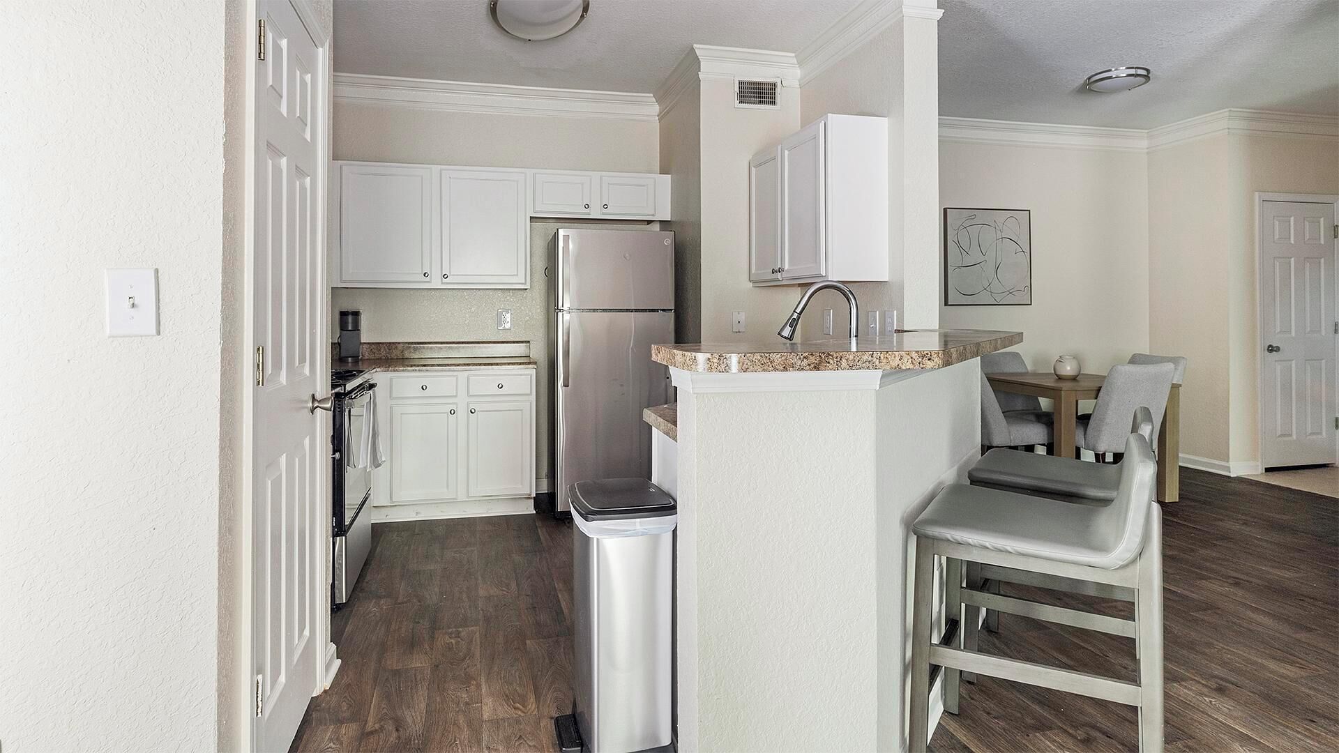 Una cocina compacta con armarios blancos, un refrigerador de acero inoxidable, un horno empotrado y una pequeña isla con pileta.