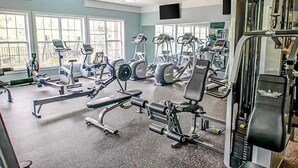 Ett gym med olika typer av träningsutrustning, stora fönster och takfläktar.