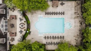 En vy från ovan över ett poolområde med solstolar, en plats för solbad och en rund bubbelpool.