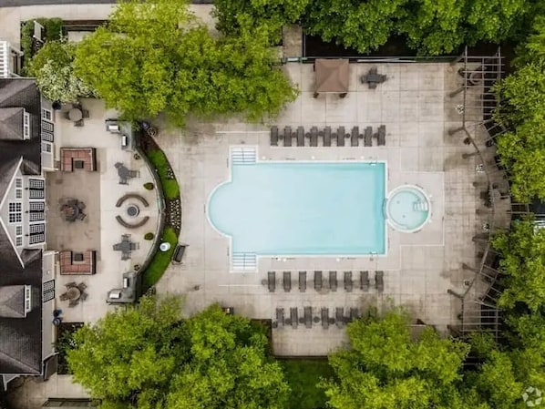 An aerial view of a swimming pool area with lounge chairs, a sunbathing area, and a circular hot tub.