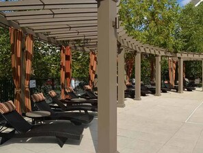 A covered outdoor seating area with lounge chairs and tables, a pergola structure, and a paved floor. - Landing | Chic 2BD, Gym, Clubhouse (King of Prussia)