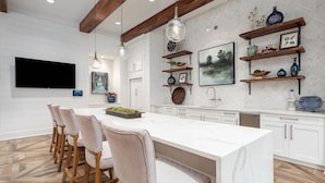 A modern kitchen with a large island, wooden chairs, pendant lights, and decorative shelves. - Landing | Incredible 2BD, Pool, Gym (Summerville)