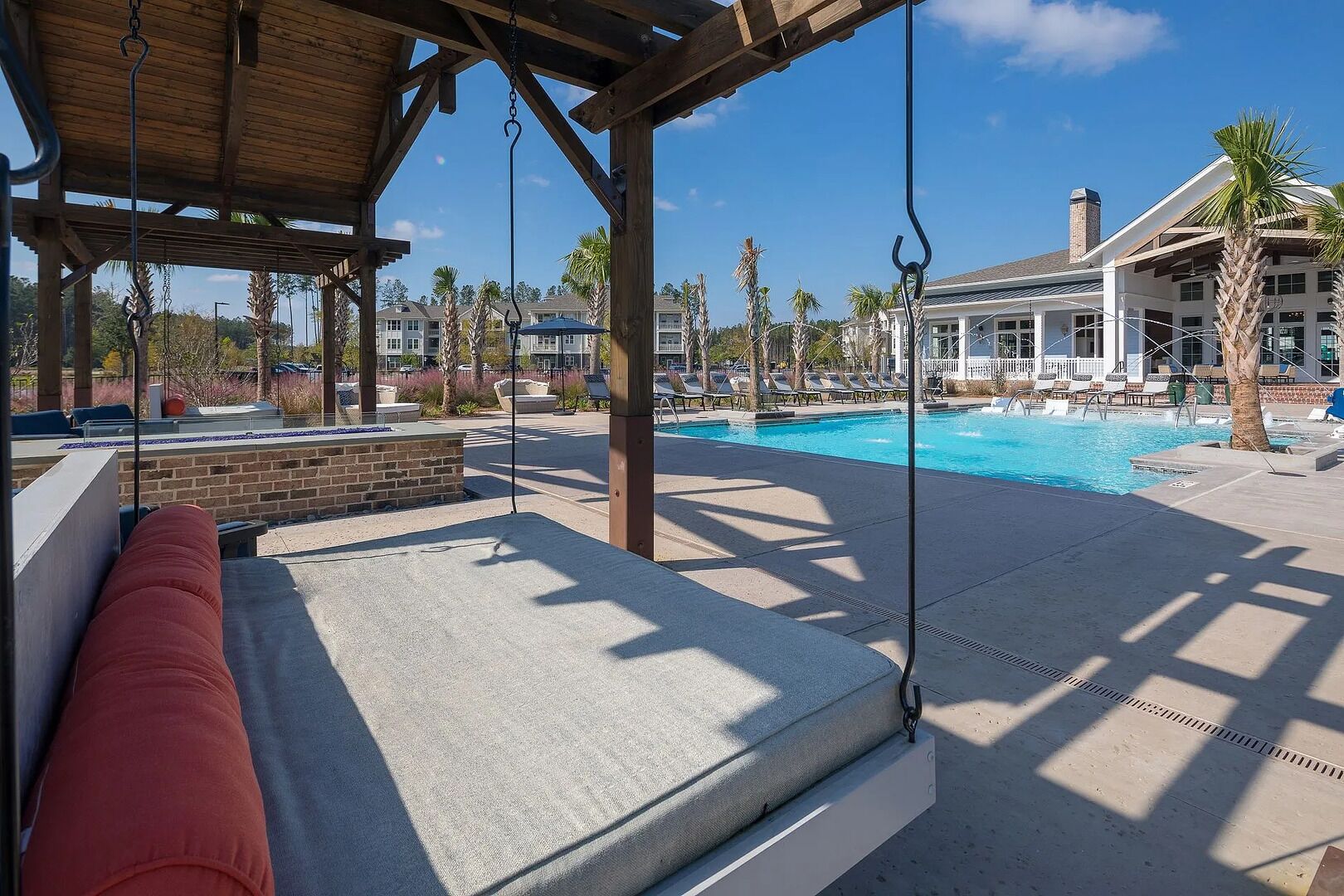 A poolside area with a swing chair, a brick planter, and a view of a residential building in the background.