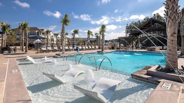A swimming pool with water features, lounge chairs, palm trees, and a building in the background. - Landing | Incredible 2BD, Pool, Gym (Summerville)