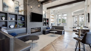 A modern living room with a fireplace, a flat-screen TV, and a dining area with a round table and chairs. - Landing | Incredible 2BD, Pool, Gym (Summerville)