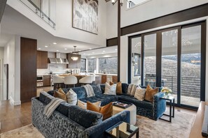 A spacious living area with a large sectional sofa, a dining table, and a kitchen in the background. - Luxe PC Estate | Chef’s Kitchen + Acreage + Views (Park City)