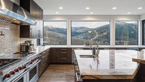 Eine moderne Küche mit einer großen Kochinsel, Edelstahlgeräten und Bergblick durch große Fenster.