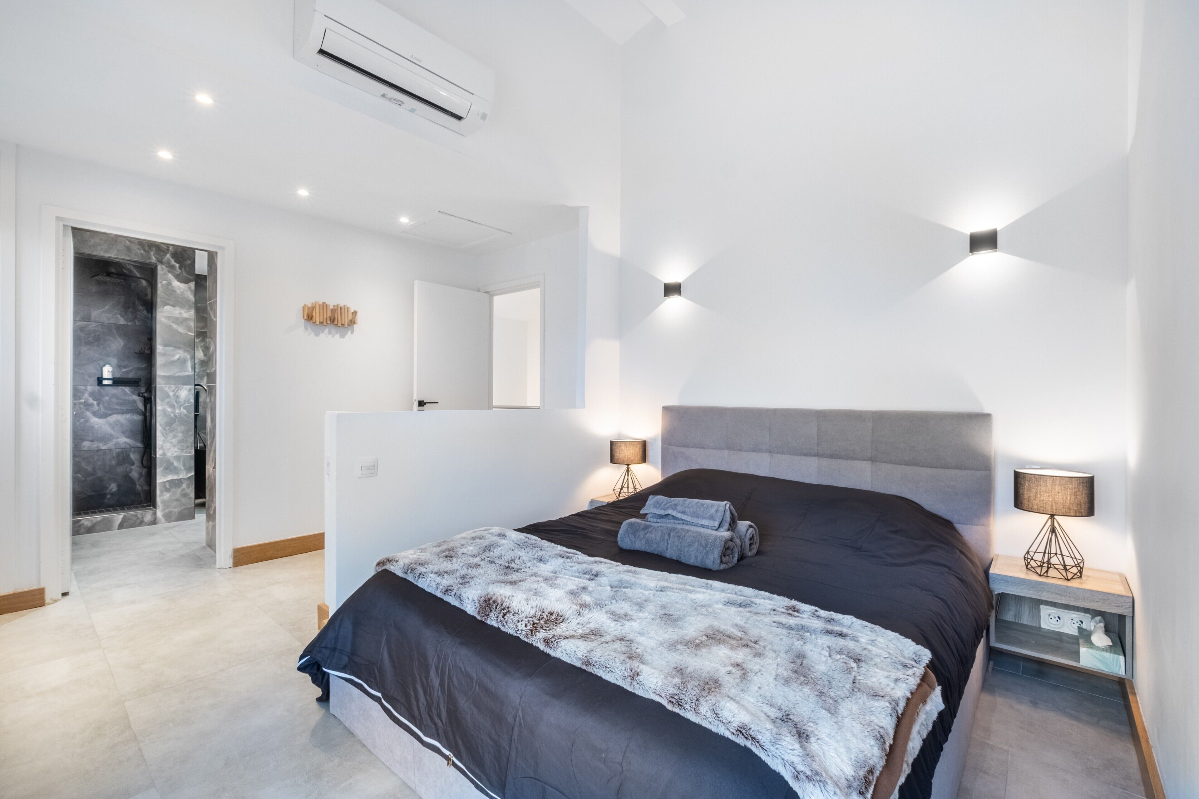 Un dormitorio moderno con una cama grande, lámparas de noche, un armario empotrado y un baño con cabina de ducha de vidrio.