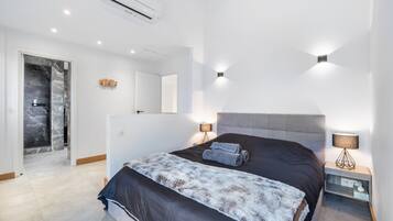 Un dormitorio moderno con una cama grande, lámparas de noche, un armario empotrado y un baño con cabina de ducha de vidrio.