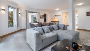 Een moderne woonkamer met een modulaire bank, eethoek en een keuken op de achtergrond.