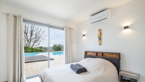Een slaapkamer met een groot bed, een glazen schuifdeur naar een zwembad en een wandairconditioner.