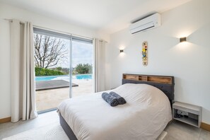 Un dormitorio con una cama grande, una puerta corrediza a una piscina y un aire acondicionado instalado en la pared.