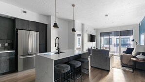 Eine moderne Küche mit einer zentralen Kochinsel, Barhocker, einem Einbaukühlschrank und einem Essbereich mit einer Couch und einem Fernseher.