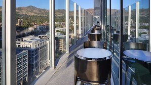 Een hoog gebouw met een glazen gevel, met panoramisch uitzicht op een stadsbeeld en bergen in de verte.