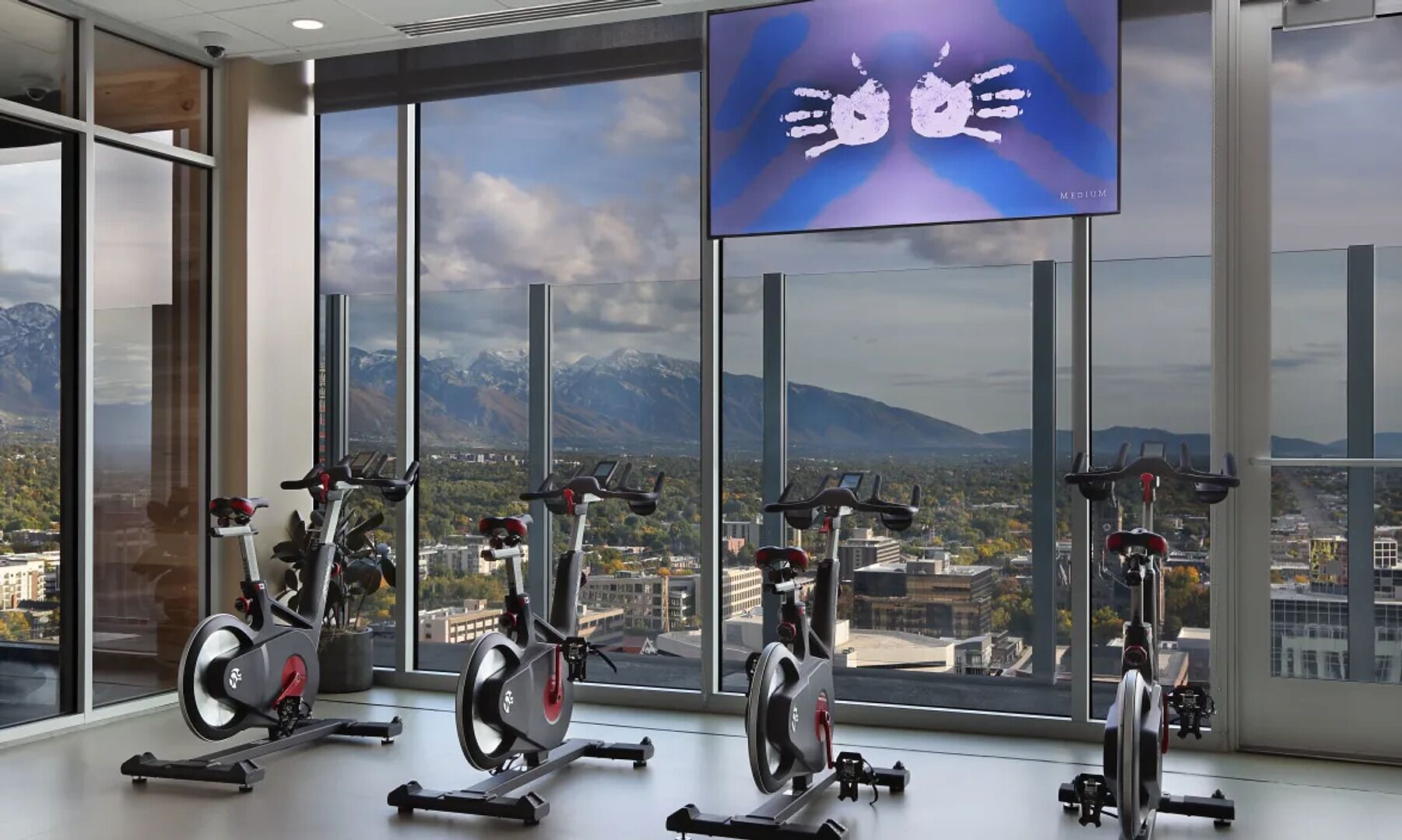 Et fitnesscenter med motionscykler, store vinduer og udsigt over bybilledet.