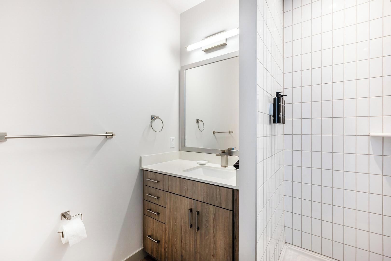 Un baño moderno con un lavamanos blanco, tocador de madera y un espejo grande.