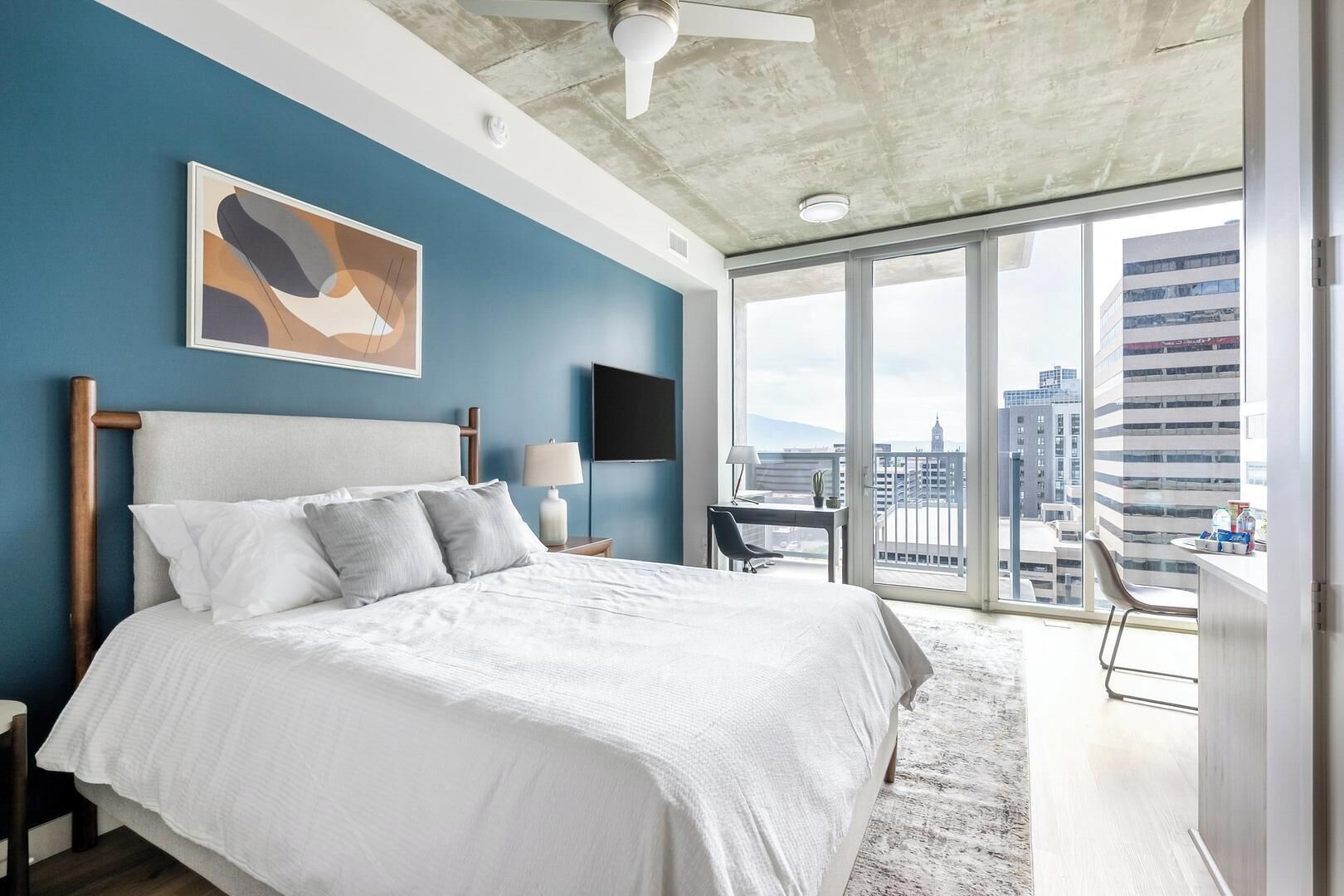 Ein modernes Hotelzimmer mit einem großen Bett, einem Schreibtisch und einem Balkon mit Blick auf die Stadt.