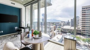 Un ufficio moderno con un'ampia finestra che offre vista sulla città, un tavolo rotondo con una pianta e un televisore a schermo piatto appeso al muro.