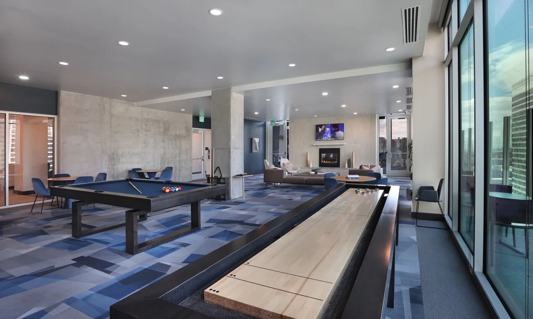 A modern indoor recreational area with pool tables, a shuffleboard table, comfortable seating, and a TV screen.