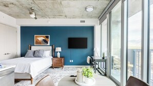 Une chambre d’hôtel moderne, équipée d’un lit, d’une table de chevet, d’une lampe et offrant une vue sur la ville grâce à de grandes fenêtres.